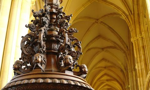 The dark wooden cover to the font has many intricate carvings, including faces.
