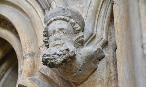 A close-up of the head and shoulders of a bearded man carved in stone.