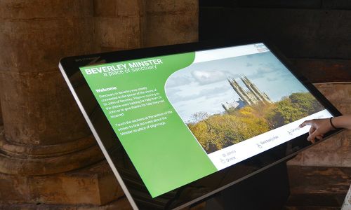 A hand interacts with a touchscreen about Beverley Minster.